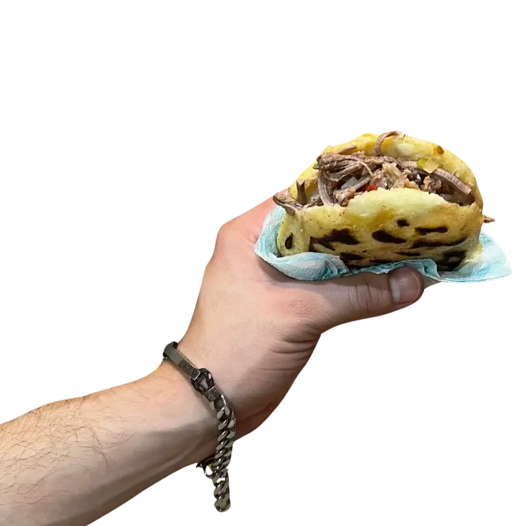Mano con una Arepa La cachonda, rellena de carne mechada. Una arepa criolla Venezolana. España, Tarragona.