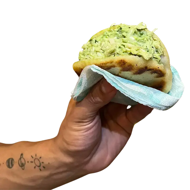 Inicio 1 Mano con una Arepa La Reina, rellena de pollo, aguacate, cebollin. Una reina pepiada Venezolana.