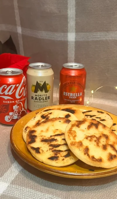 A plate with arepas, along with a Coca-Cola, Estrella Damm and Estrella Damm lemon. Surrounded by a Christmas flower.