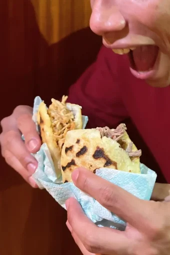 Boy eating two arepas, one with meat and one with chicken.